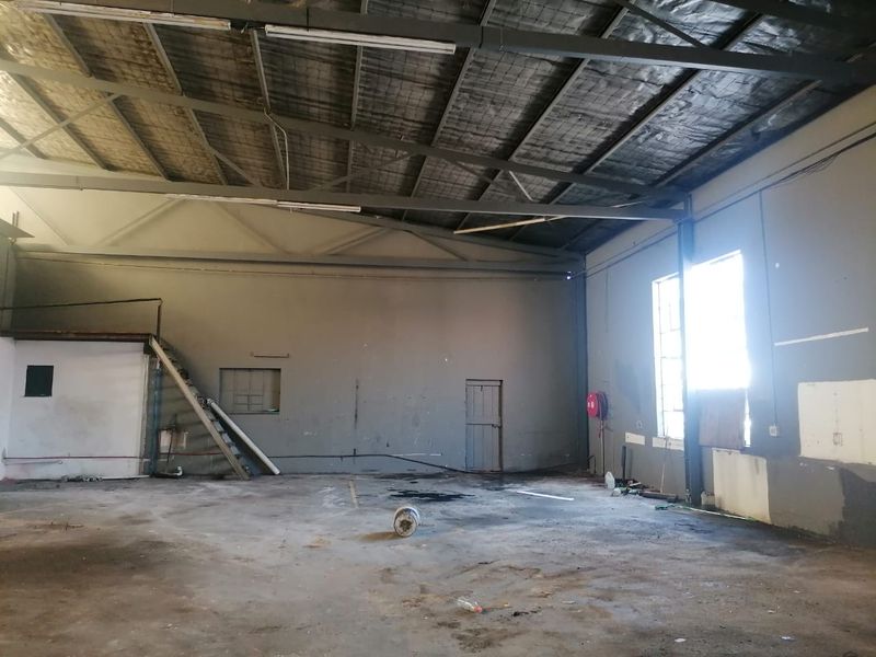 Spacious industrial utility area featuring exposed steel roof trusses, concrete flooring, and a mezzanine access ladder, suitable for warehouse or workshop use.