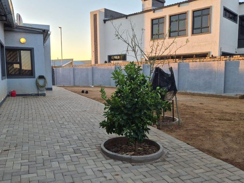 Rear exterior view featuring a paved walkway, perimeter wall, and an open garden area with potential for landscaping.