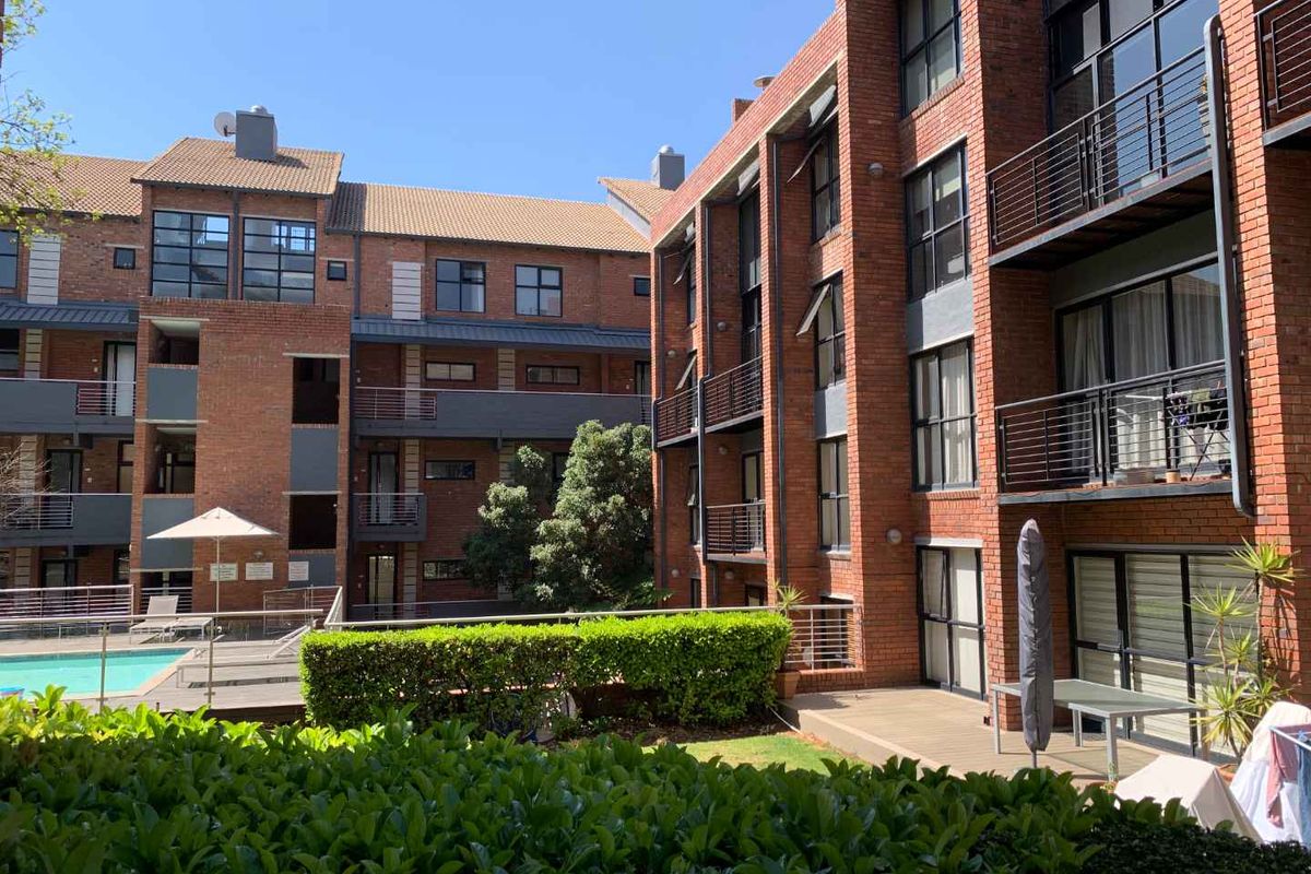 View of the apartment complex exterior featuring face brick architecture, private balconies, and a communal swimming pool area with landscaped gardens.