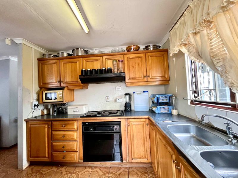 A functional kitchen featuring traditional wooden cabinetry, built-in oven, electric hob, and a double bowl stainless steel sink with tiled flooring.