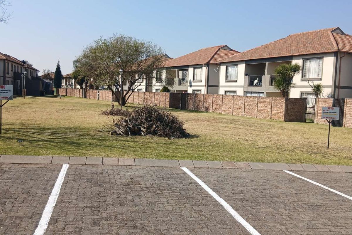 A view of the communal garden area and paved parking bays within the apartment complex, featuring brick boundary walls and residential building facades.