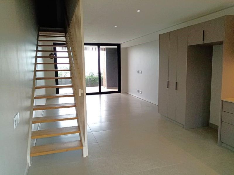 Modern open-plan living area featuring a timber staircase, sleek built-in cabinetry, tiled flooring, and large sliding glass doors leading to an outdoor space.