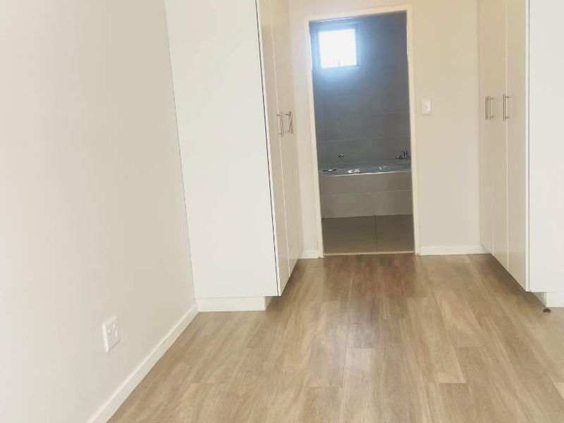 A clean, empty bedroom featuring light-toned laminate flooring and ample built-in cupboard storage, with an adjacent bathroom visible through the doorway.