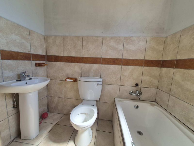 A functional bathroom featuring a pedestal basin, toilet, and bathtub with neutral wall and floor tiling, requiring some cosmetic updates.