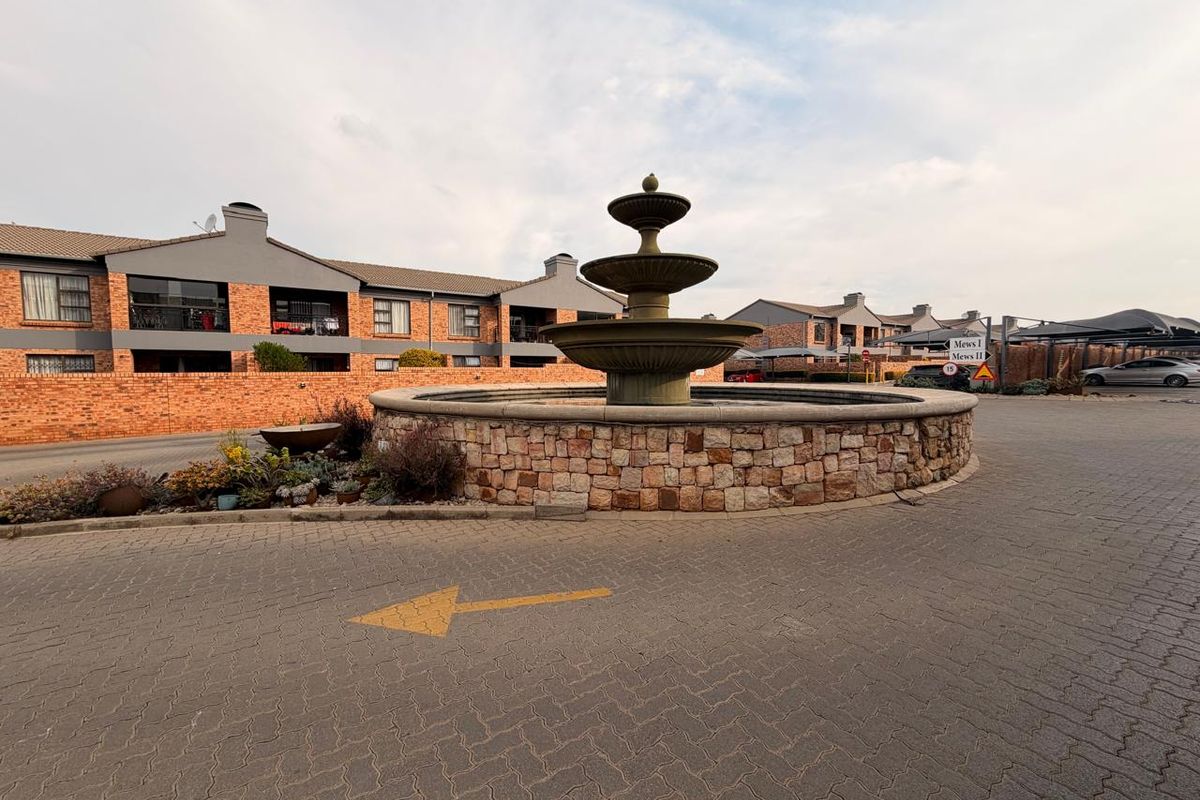 A view of the apartment complex entrance featuring a central stone-clad fountain and paved driveway area.