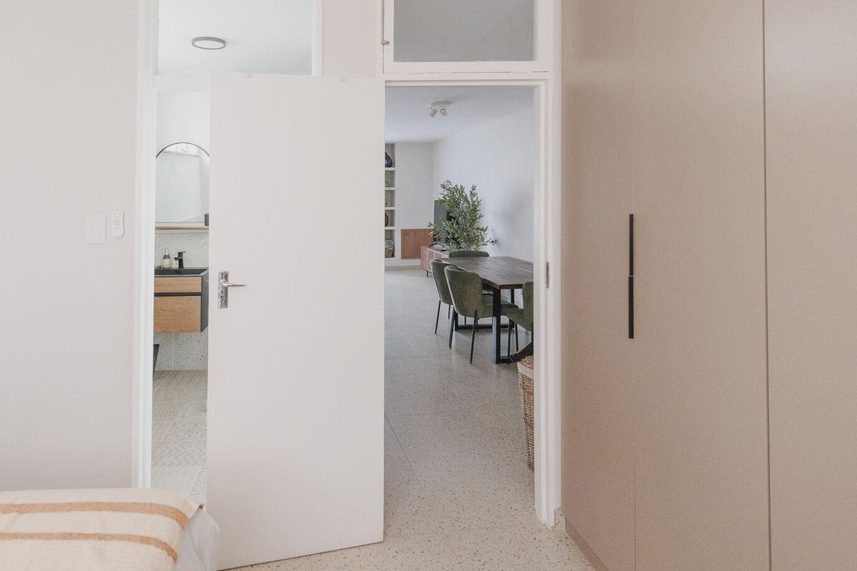 A modern bedroom featuring sleek built-in wardrobes, terrazzo flooring, and a view through to the adjoining bathroom and living area.