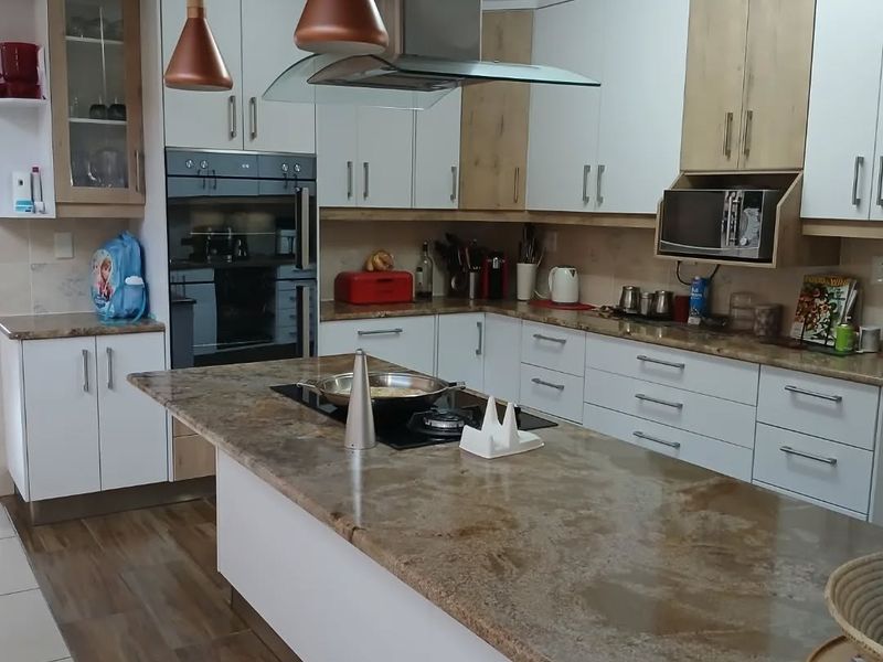 Modern kitchen featuring a large central island with stone countertops, built-in oven, integrated hob, extractor fan, and ample white and wood-tone cabinetry.