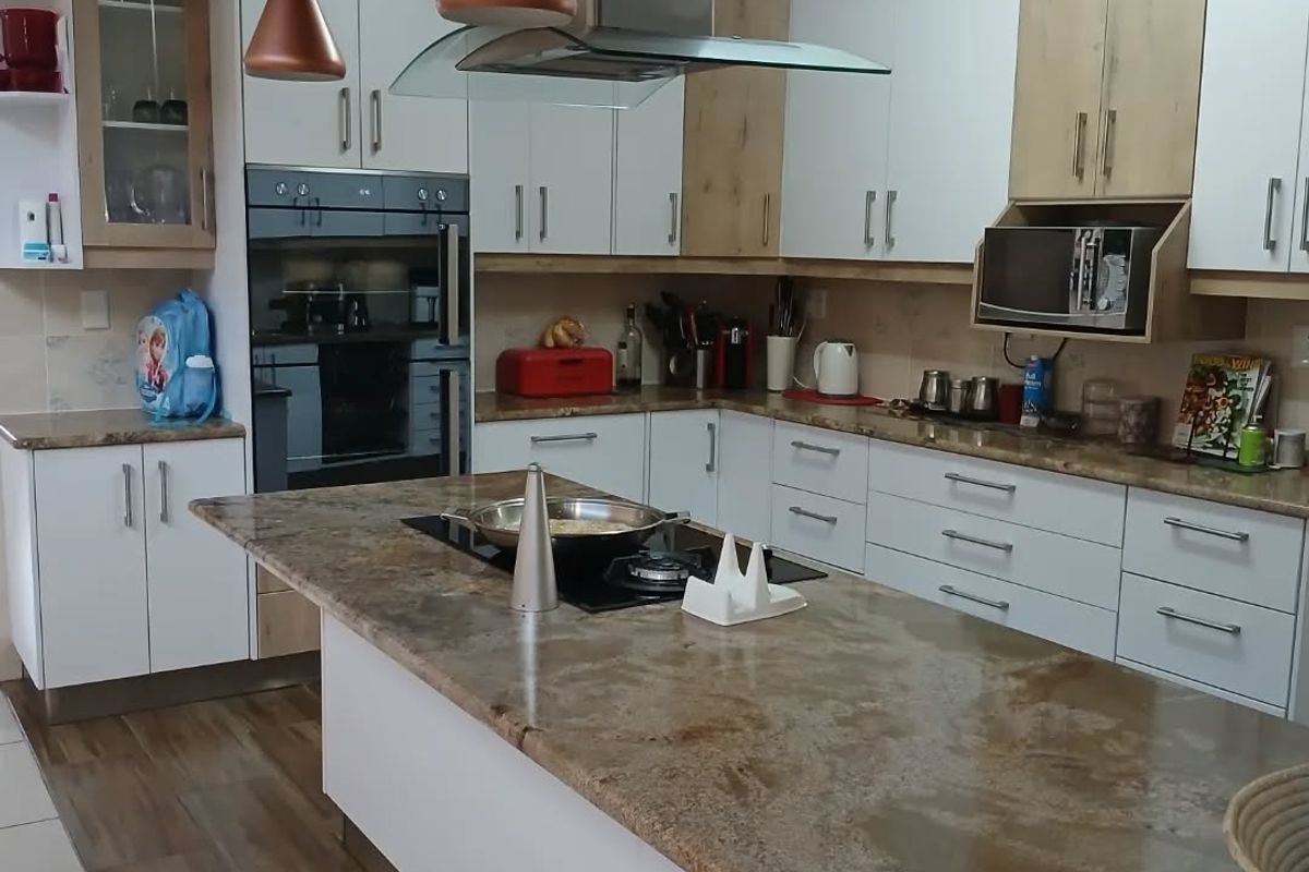 Modern kitchen featuring a large central island with stone countertops, built-in oven, integrated hob, extractor fan, and ample white and wood-tone cabinetry.