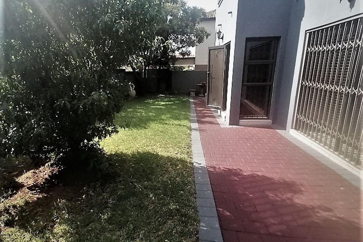 A rear exterior view featuring a paved walkway alongside a lawn and the side elevation of the house with security gates.