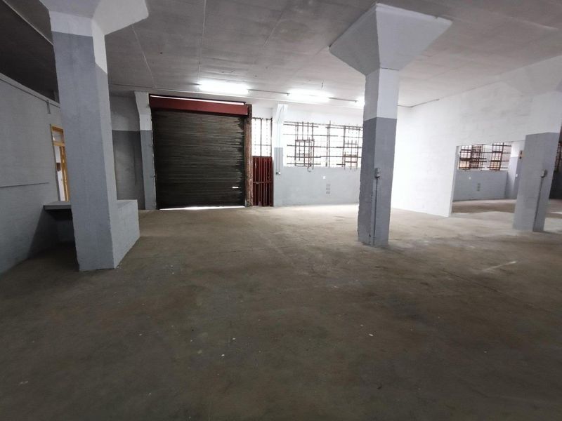 Spacious industrial utility area featuring concrete flooring, structural columns, and a large roller shutter door for easy access.