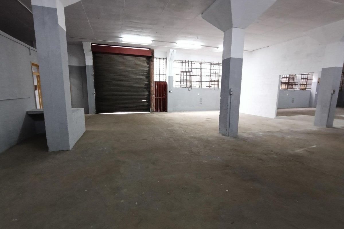 Spacious industrial utility area featuring concrete flooring, structural columns, and a large roller shutter door for easy access.