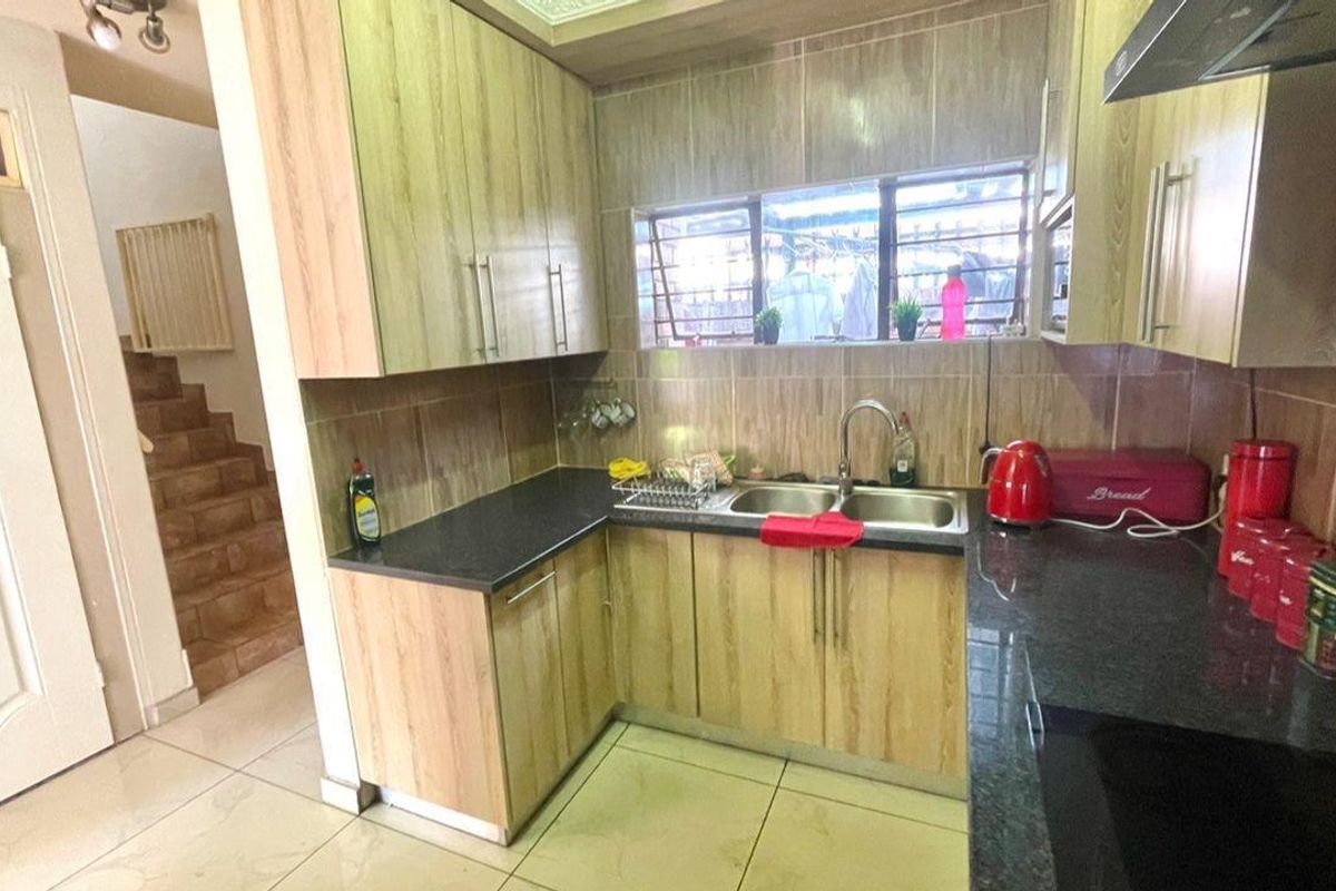 A functional kitchen featuring wood-look cabinetry, dark granite countertops, a double-basin sink, and tiled flooring, with an adjacent staircase visible.