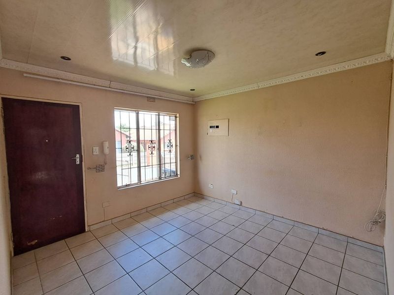 An empty living area featuring tiled flooring, security window bars, and an integrated intercom system, ready for a fresh coat of paint.