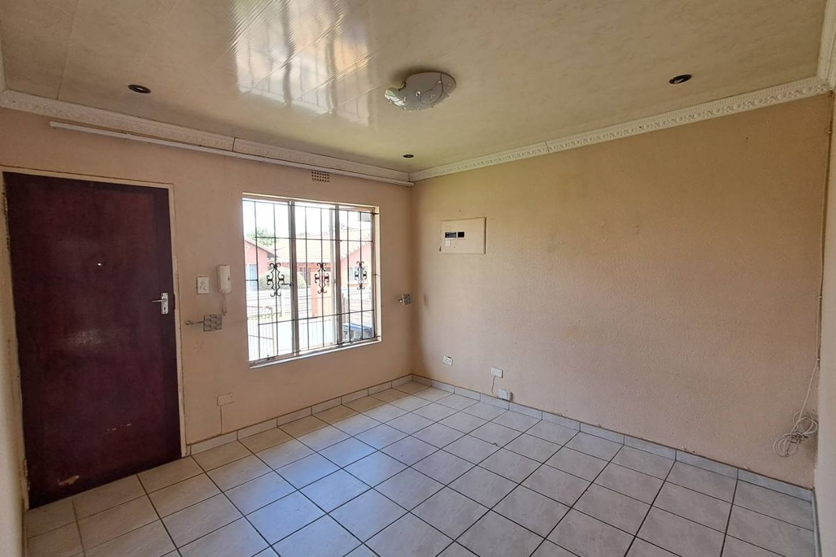 An empty living area featuring tiled flooring, security window bars, and an integrated intercom system, ready for a fresh coat of paint.