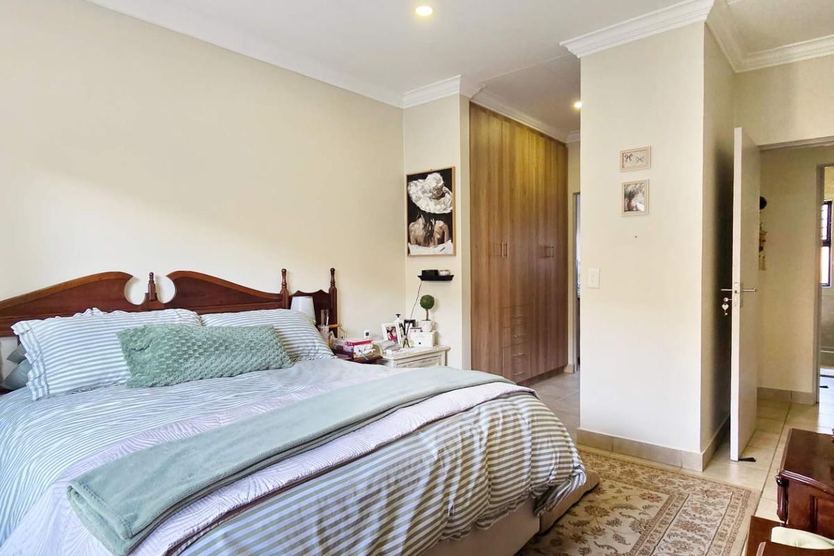 A well-maintained bedroom featuring built-in wooden cupboards, crown molding, and an en-suite bathroom with a shower.