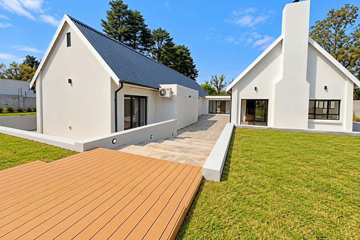 Modern rear exterior view featuring a white facade, metal roof, chimney, timber decking, and a well-maintained lawn with paved access.