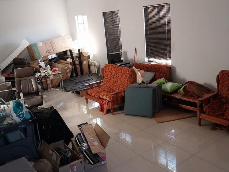 A spacious industrial-style room featuring tiled flooring, fluorescent lighting, and venetian blinds, currently utilized as a storage and living area.