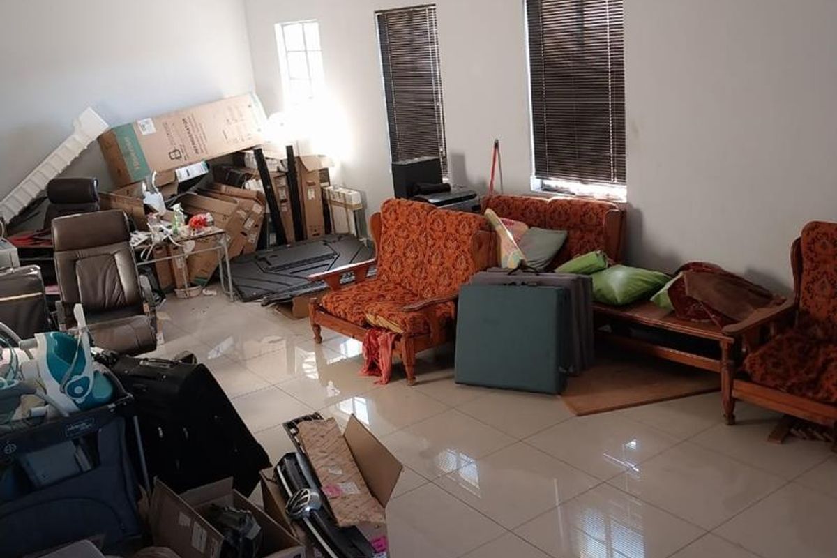 A spacious industrial-style room featuring tiled flooring, fluorescent lighting, and venetian blinds, currently utilized as a storage and living area.