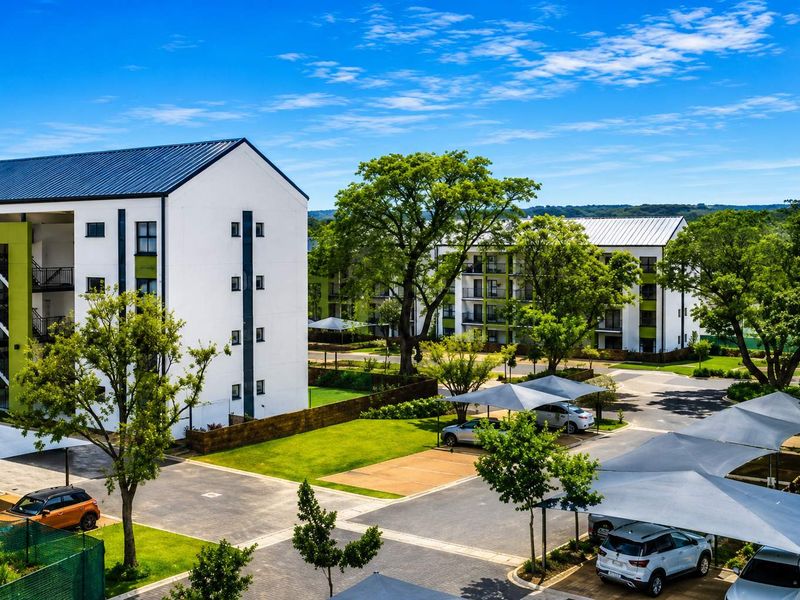 An elevated view of a modern apartment complex featuring well-maintained landscaped gardens, paved parking areas, and shade cloth carports.