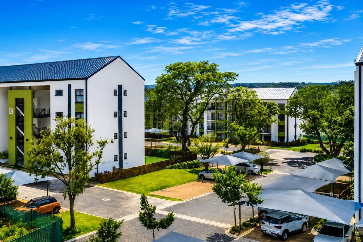 An elevated view of a modern apartment complex featuring well-maintained landscaped gardens, paved parking areas, and shade cloth carports.