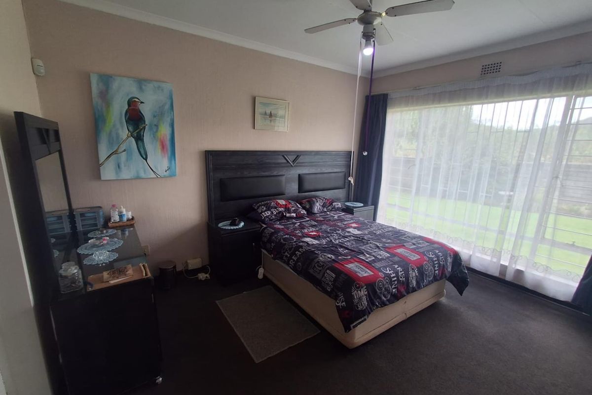 A bedroom featuring a ceiling fan, large sliding glass doors with garden views, and carpeted flooring.