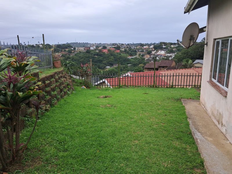 Rear garden area featuring a lawn, retaining wall, and metal fencing with an elevated view of the surrounding neighborhood.