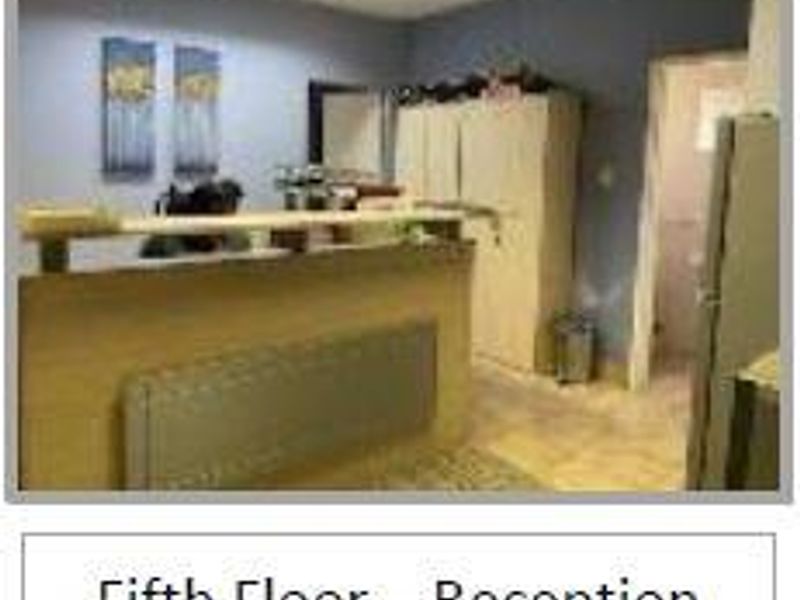 A functional office reception area featuring a built-in desk, overhead fluorescent lighting, and storage cabinetry.