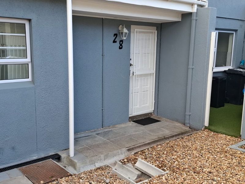 Front entrance of the apartment featuring a security gate, tiled porch area, and low-maintenance gravel landscaping.