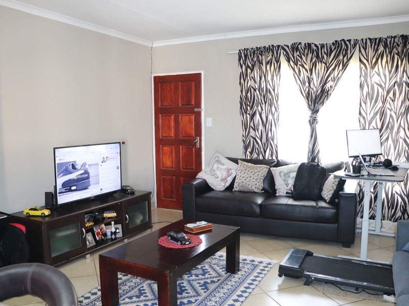 A functional living room featuring tiled flooring, a solid timber door, and neutral wall finishes, providing a comfortable and versatile living space.