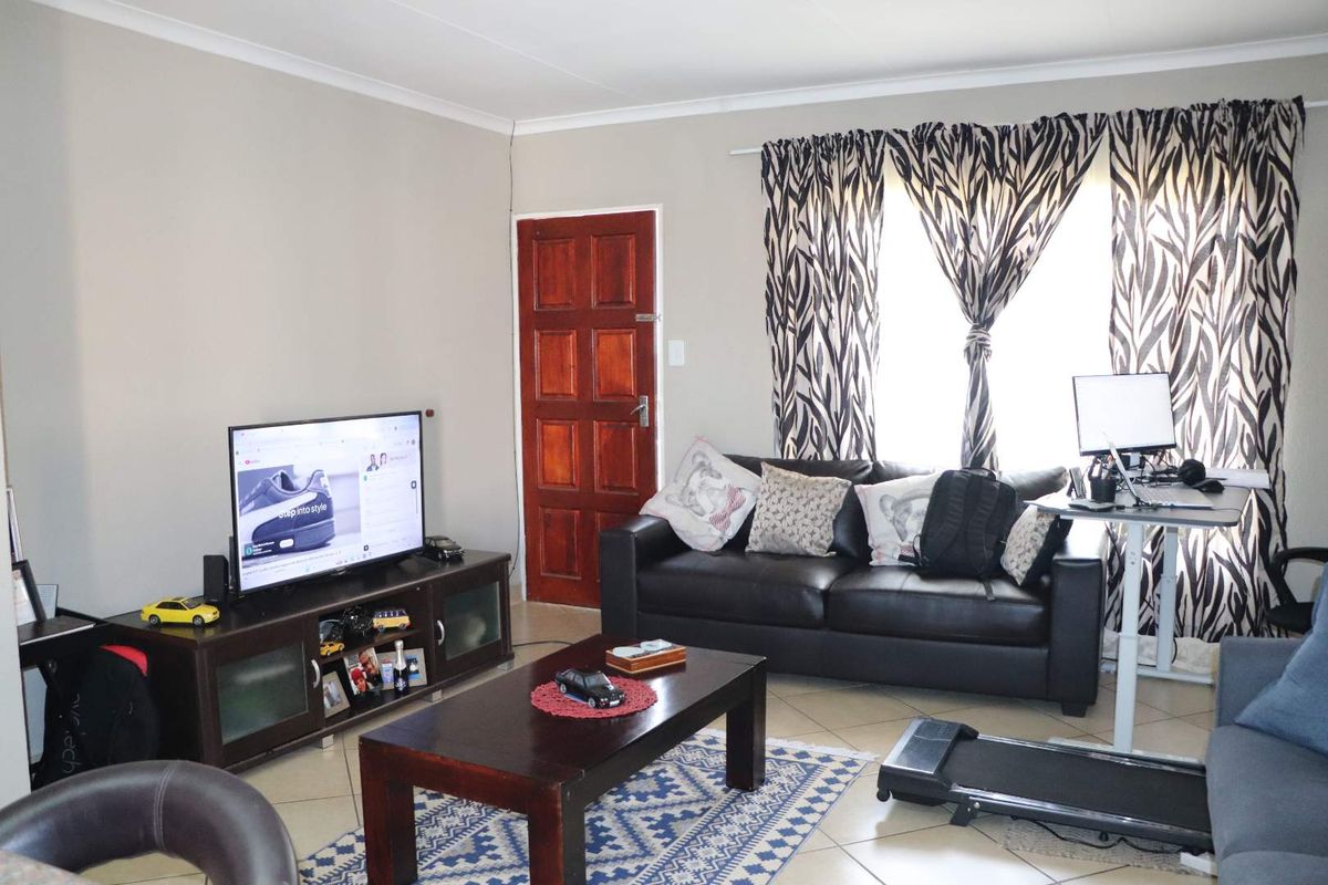 A functional living room featuring tiled flooring, a solid timber door, and neutral wall finishes, providing a comfortable and versatile living space.
