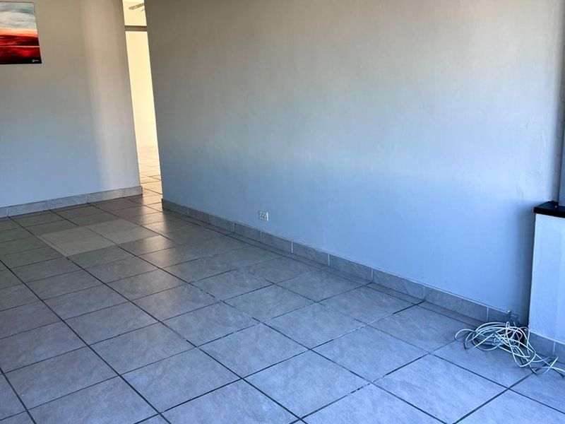 An empty living area featuring neutral tiled flooring and a ceiling fan, offering a blank canvas for interior design.