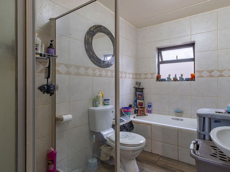 A functional bathroom featuring a shower enclosure, bathtub, toilet, and tiled finishes. The space would benefit from cosmetic updates to modernize the fixtures.
