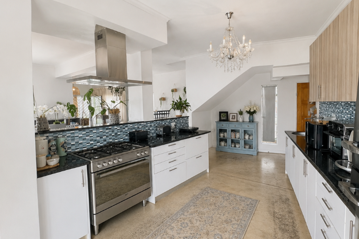 Modern kitchen featuring polished concrete floors, granite countertops, mosaic tile backsplash, and a stainless steel gas range with an overhead extractor fan.