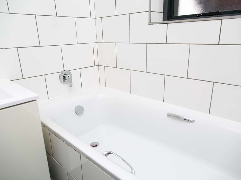 A clean bathroom featuring a built-in bathtub with chrome fixtures and white subway wall tiling.