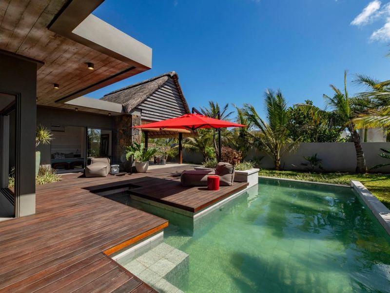 A modern outdoor living area featuring a timber deck, a swimming pool with integrated steps, and a covered patio space.