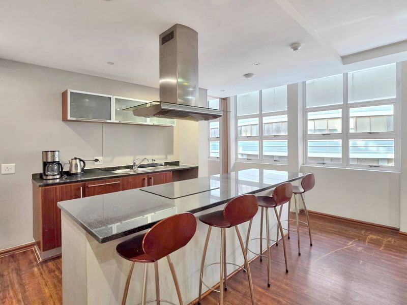 Modern kitchen featuring a central island with a built-in hob, granite countertops, stainless steel extractor fan, and ample natural light from large windows.