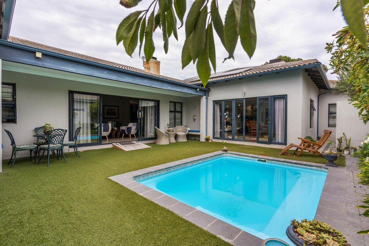 A well-maintained rear courtyard featuring a swimming pool, artificial lawn, and covered patio area with large sliding glass doors leading into the home.
