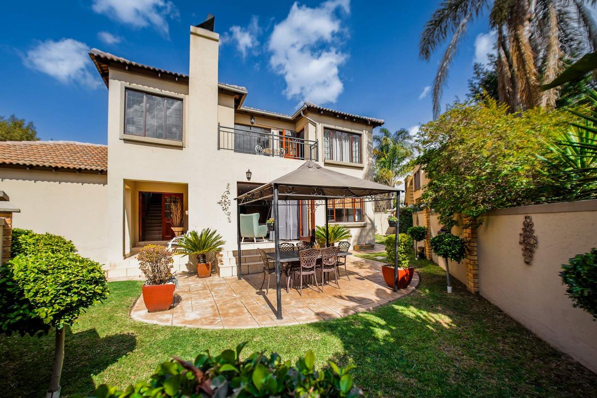 Rear view of the townhouse featuring a paved patio area, a private garden, and an upper-level balcony with a chimney stack.