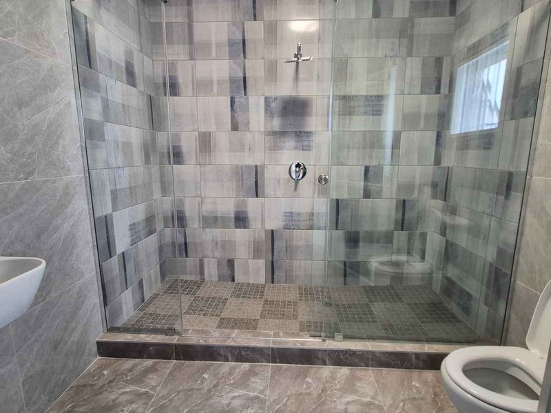 Modern bathroom featuring a spacious walk-in shower with glass screen, contemporary wall-hung basin, and stylish grey-toned tiled finishes throughout.