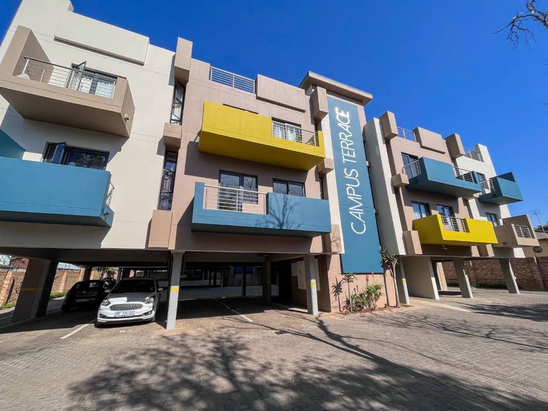 Modern apartment building facade featuring colorful balconies, covered ground-level parking, and paved driveway access.