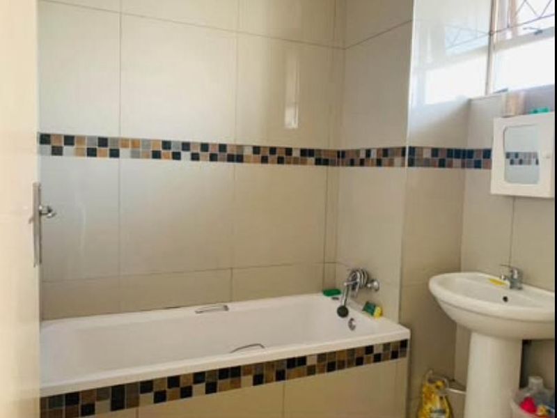 A functional bathroom featuring a standard bathtub, pedestal basin, and neutral wall tiling with a decorative mosaic accent border.