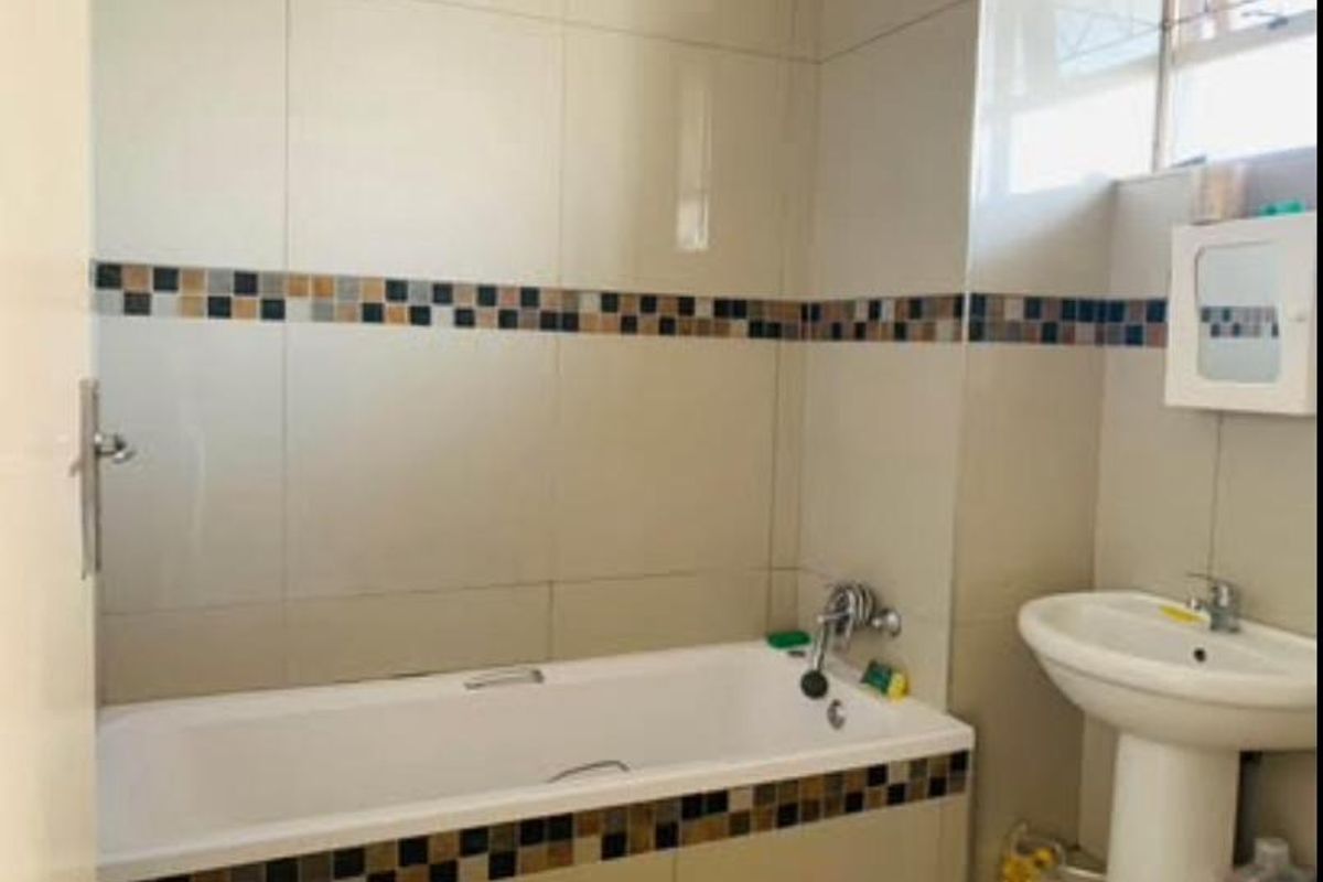 A functional bathroom featuring a standard bathtub, pedestal basin, and neutral wall tiling with a decorative mosaic accent border.