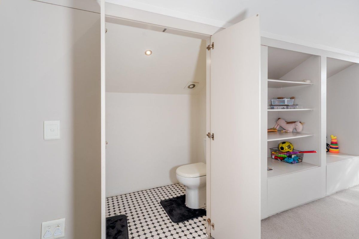 A compact, functional bathroom featuring a toilet and built-in shelving, finished with classic monochrome mosaic floor tiling.