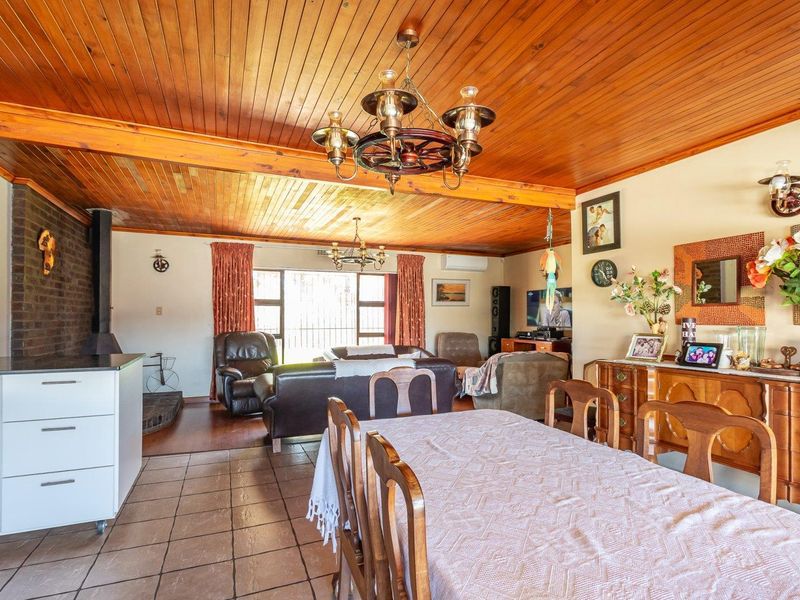 Spacious open-plan living and dining area featuring a warm timber ceiling, exposed brick feature wall, and a functional freestanding fireplace.
