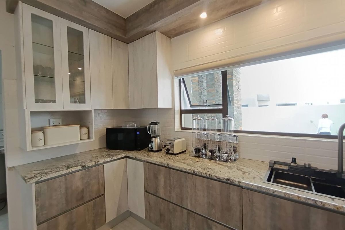 Modern kitchen featuring stone countertops, two-tone cabinetry, integrated sink, and large window providing natural light.
