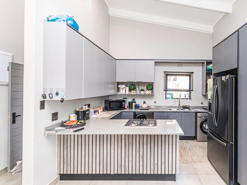 Modern kitchen featuring sleek grey cabinetry, stone countertops, a gas hob, and a vaulted ceiling, providing a functional and contemporary cooking space.