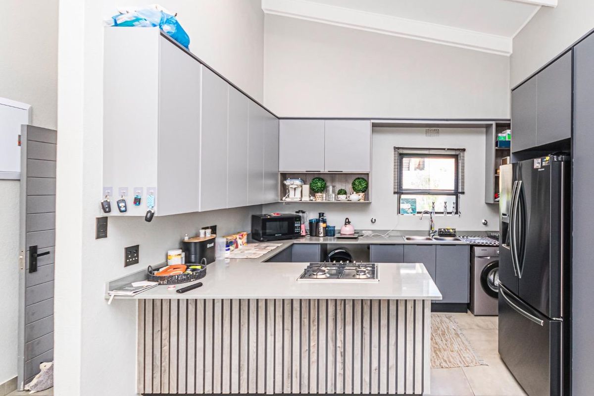Modern kitchen featuring sleek grey cabinetry, stone countertops, a gas hob, and a vaulted ceiling, providing a functional and contemporary cooking space.