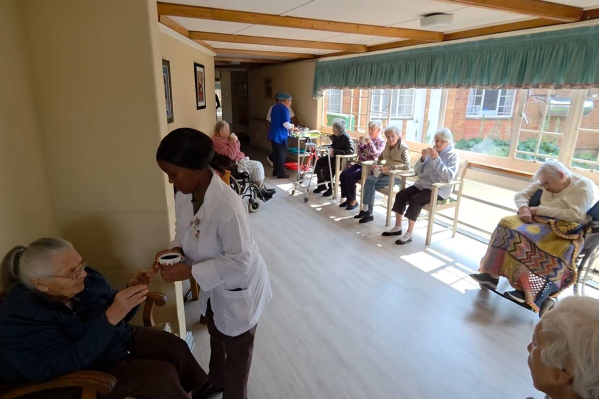 A communal living area featuring large windows, laminate flooring, and exposed beam ceilings, currently utilized as a shared space for residents.