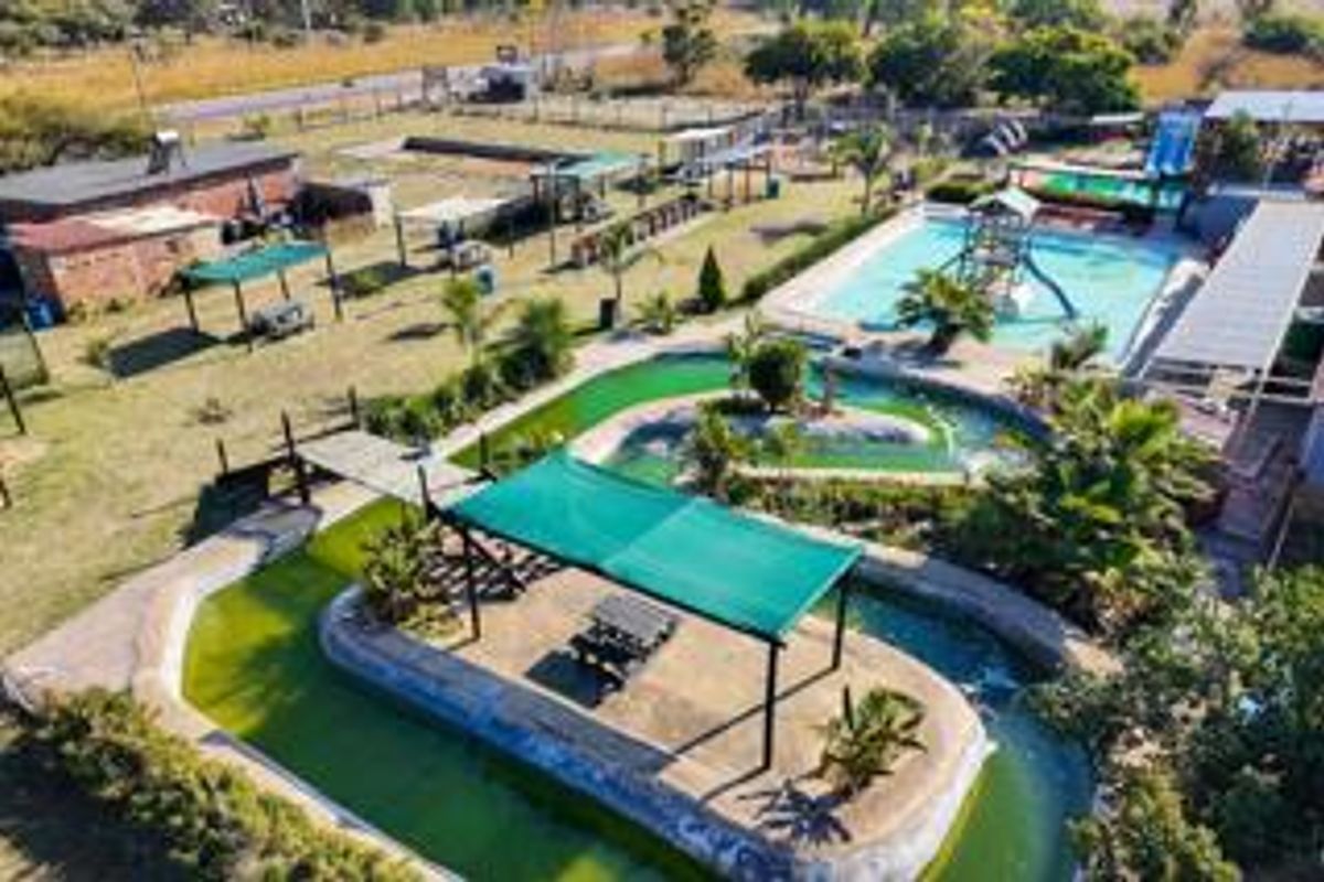 Aerial view of a small holding property featuring multiple swimming pools, water features, and outdoor shade structures set within a landscaped garden area.