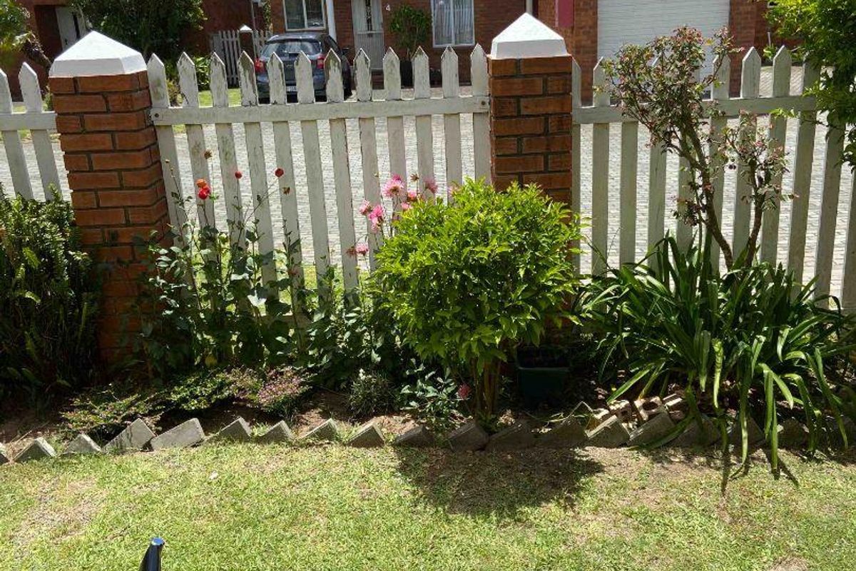 A view of a private rear garden featuring a lawn, landscaped flower beds, a brick and picket fence boundary, and a tiled patio area.